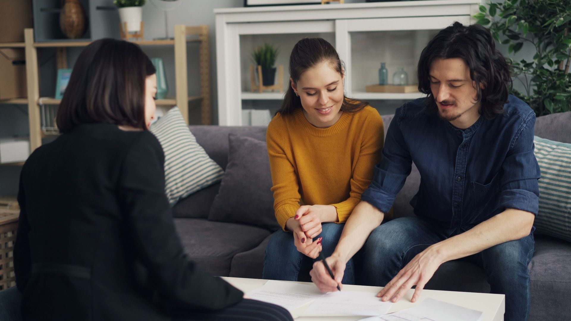 Three young adults working together at a home setting, signing documents.