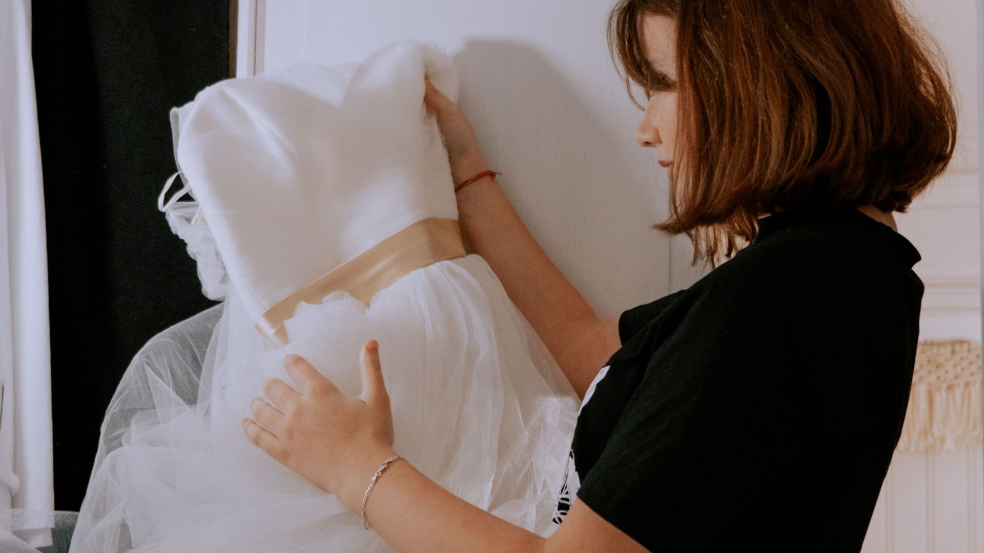 A young woman closely examines a beautiful wedding dress inside a room.