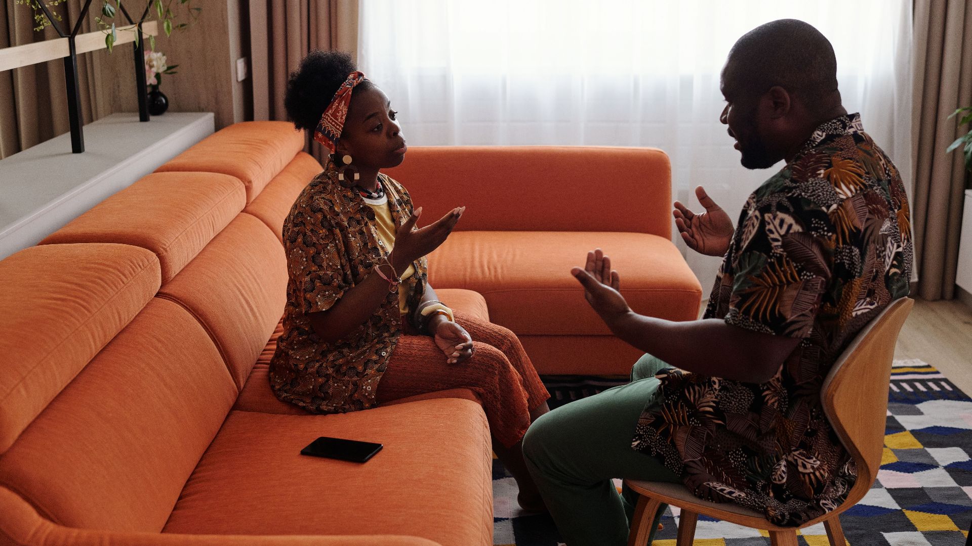 A couple having an emotional discussion on an orange sofa in modern living room.
