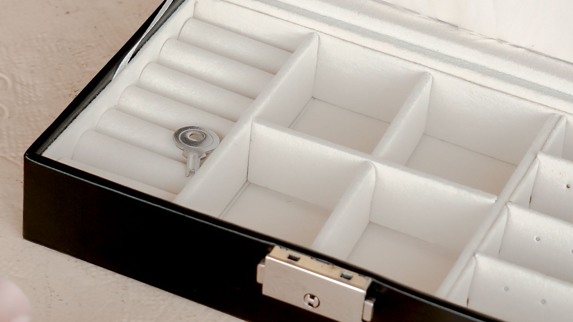 Open black jewelry box with white interior on a white surface, adorned with roses.