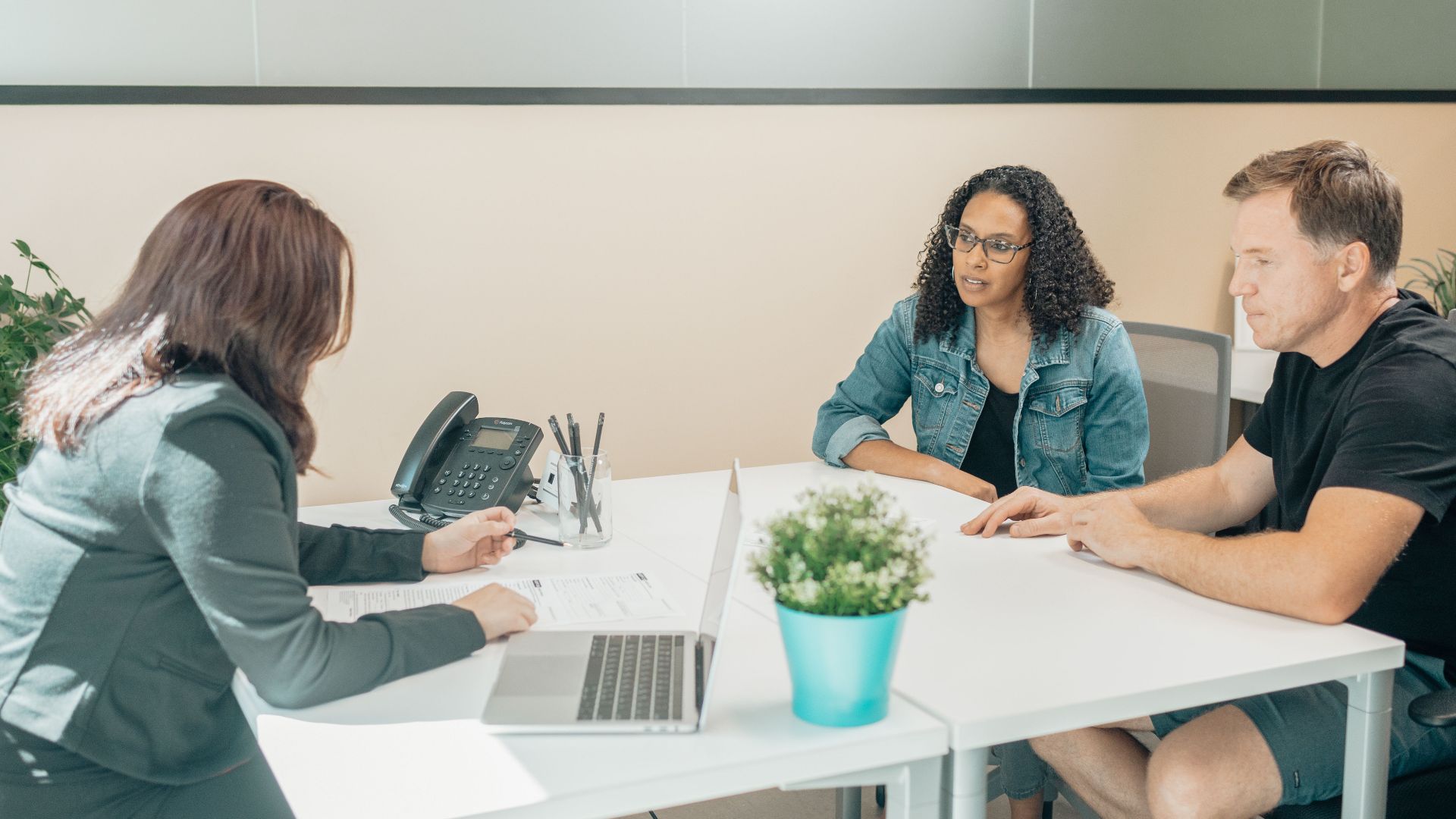Anonymous female employee interacting with diverse clients at table with netbook and paper sheet in workspace