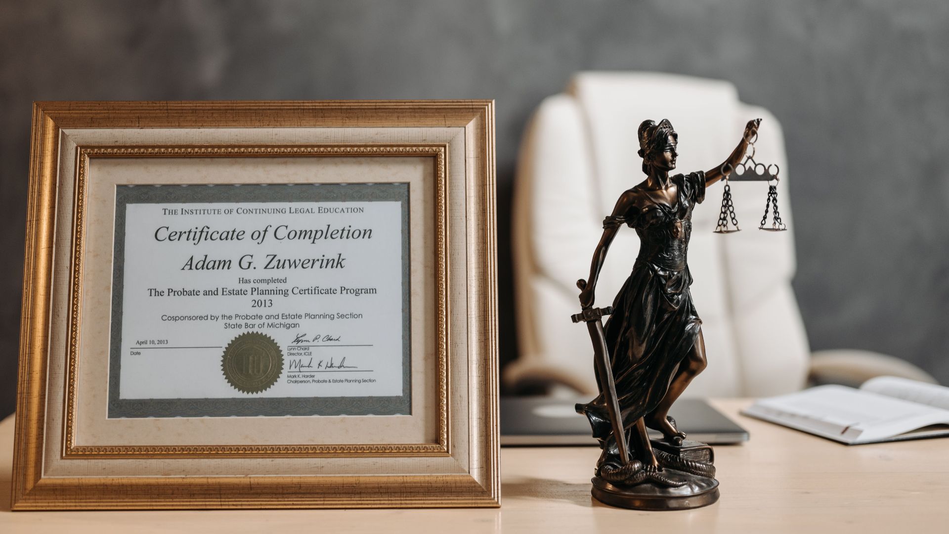 A framed legal certificate and Lady Justice figurine on a desk in a law office setting.