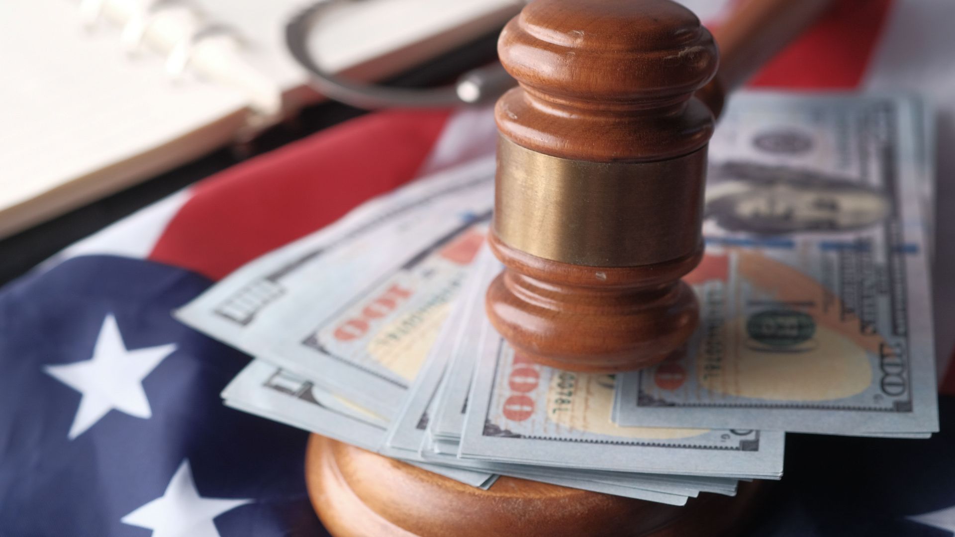 Close-up of a judge's gavel resting on US dollar bills and an American flag, symbolizing justice and finance.