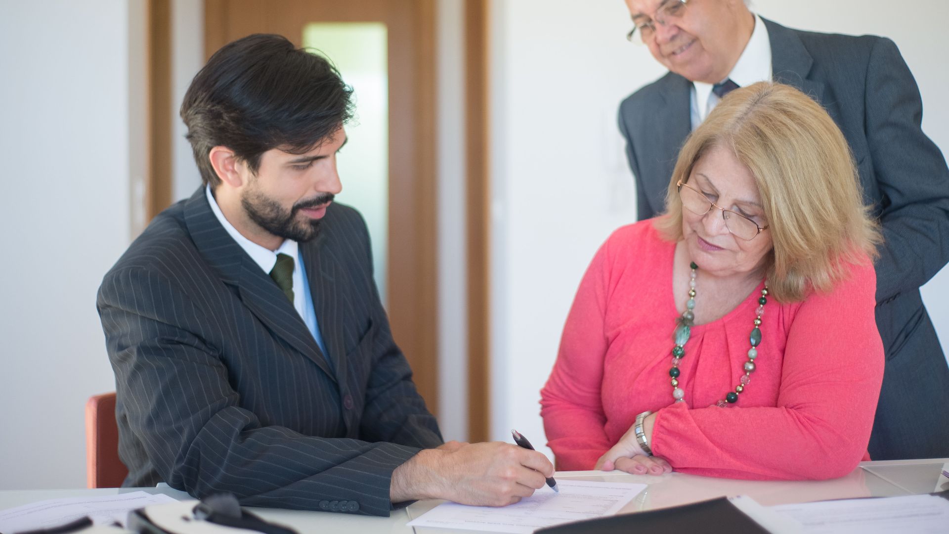Senior couple signing real estate documents with an agent in a modern office setting.