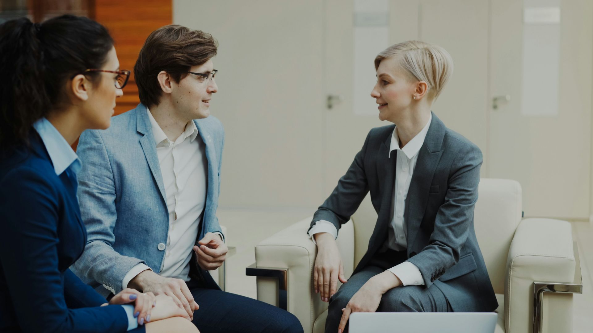 Three professionals in business attire conversing indoors.