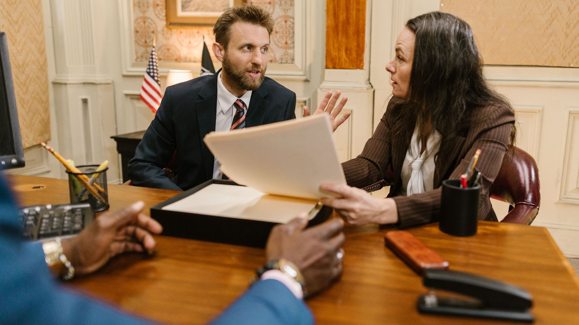 Diverse group in a corporate office engaged in a formal meeting. Professional attire and documents suggest a business discussion.