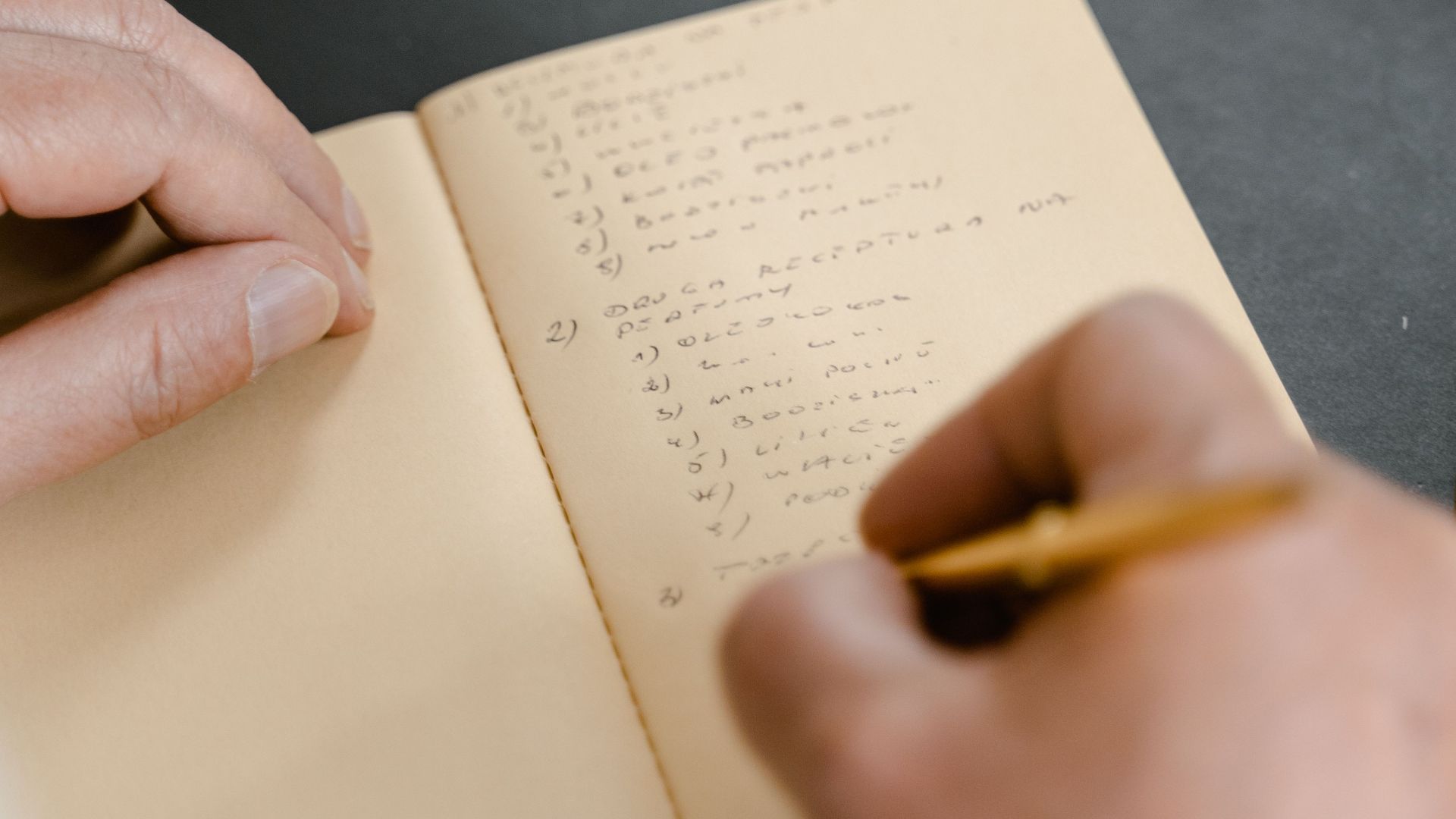 A person writing in a notebook with a pencil, focusing on note-taking.