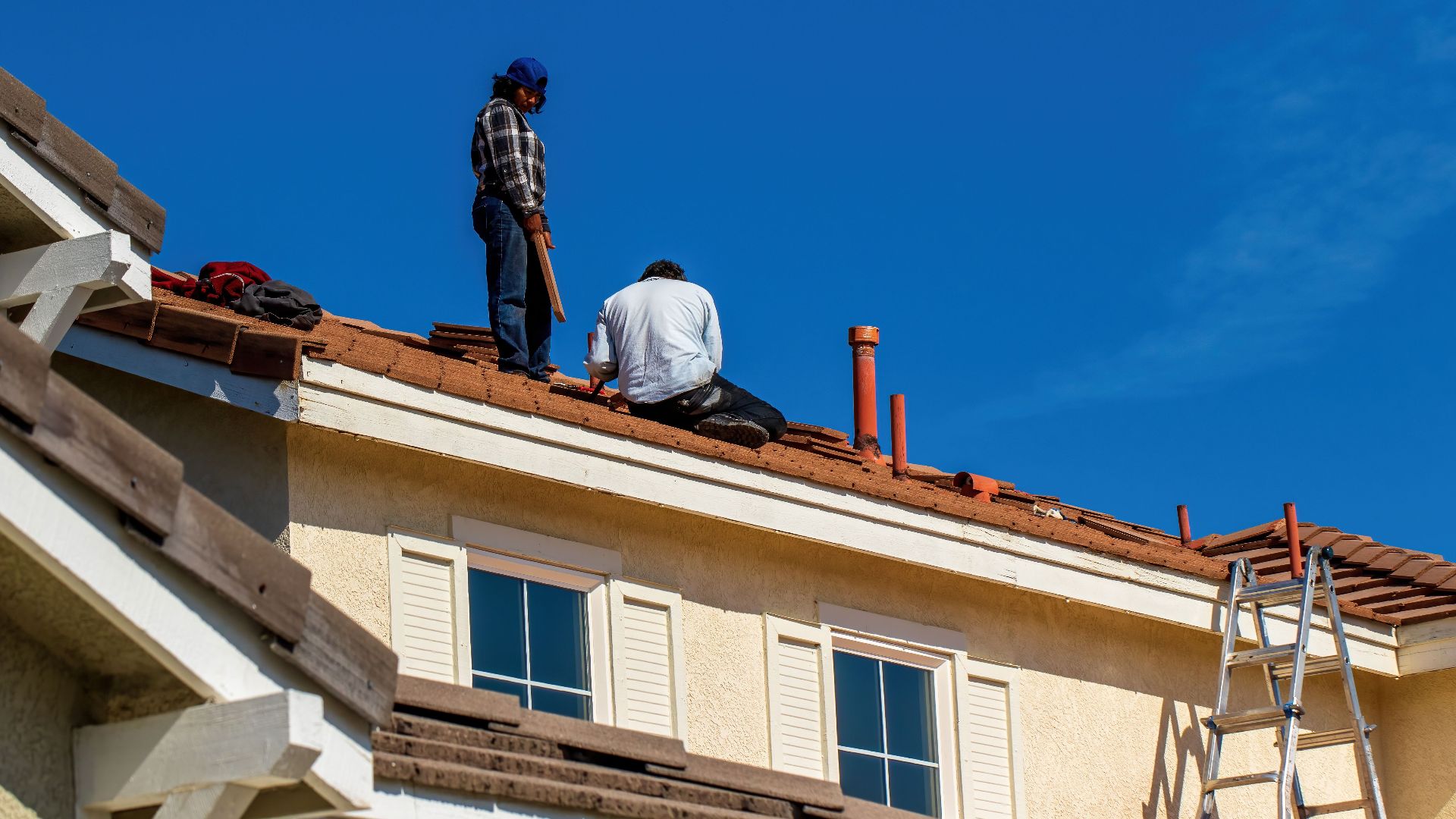 Roof construction scene with workers on a tiled roof, captured under a clear blue sky.