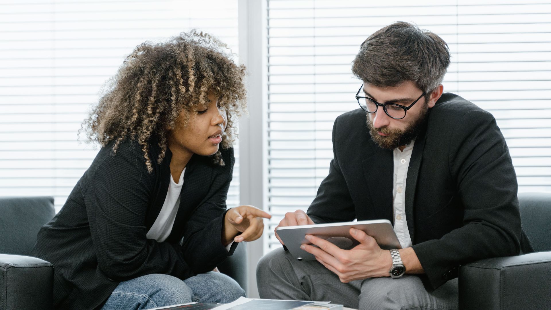 Two colleagues in a business setting discussing ideas using a tablet for planning.