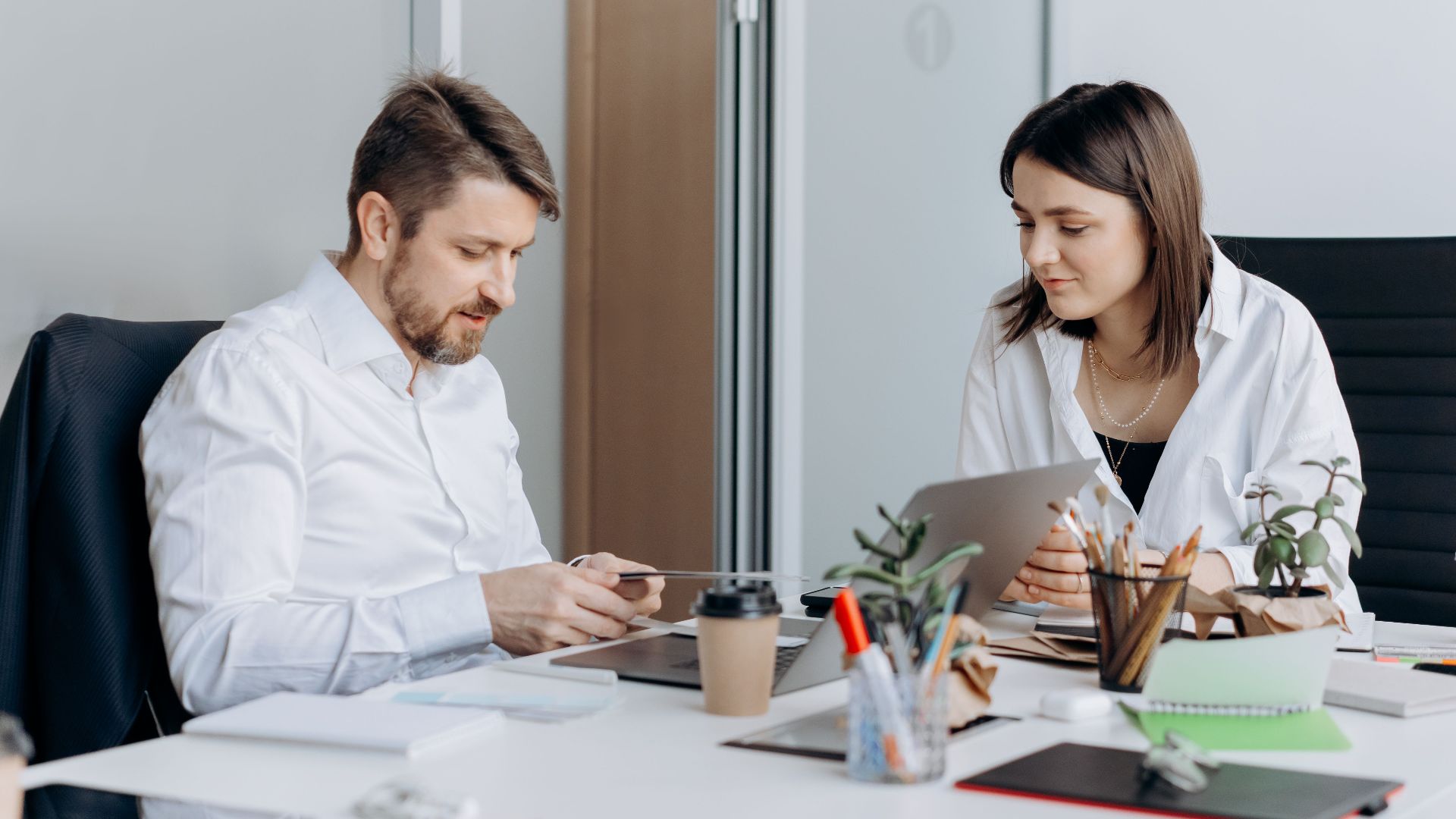 Two colleagues engaged in discussion at a well-equipped modern office workspace with laptops and papers.