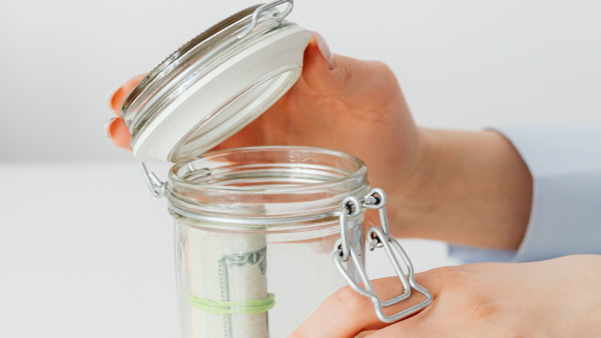Close-up of hands placing money into a jar, symbolizing savings and financial planning.