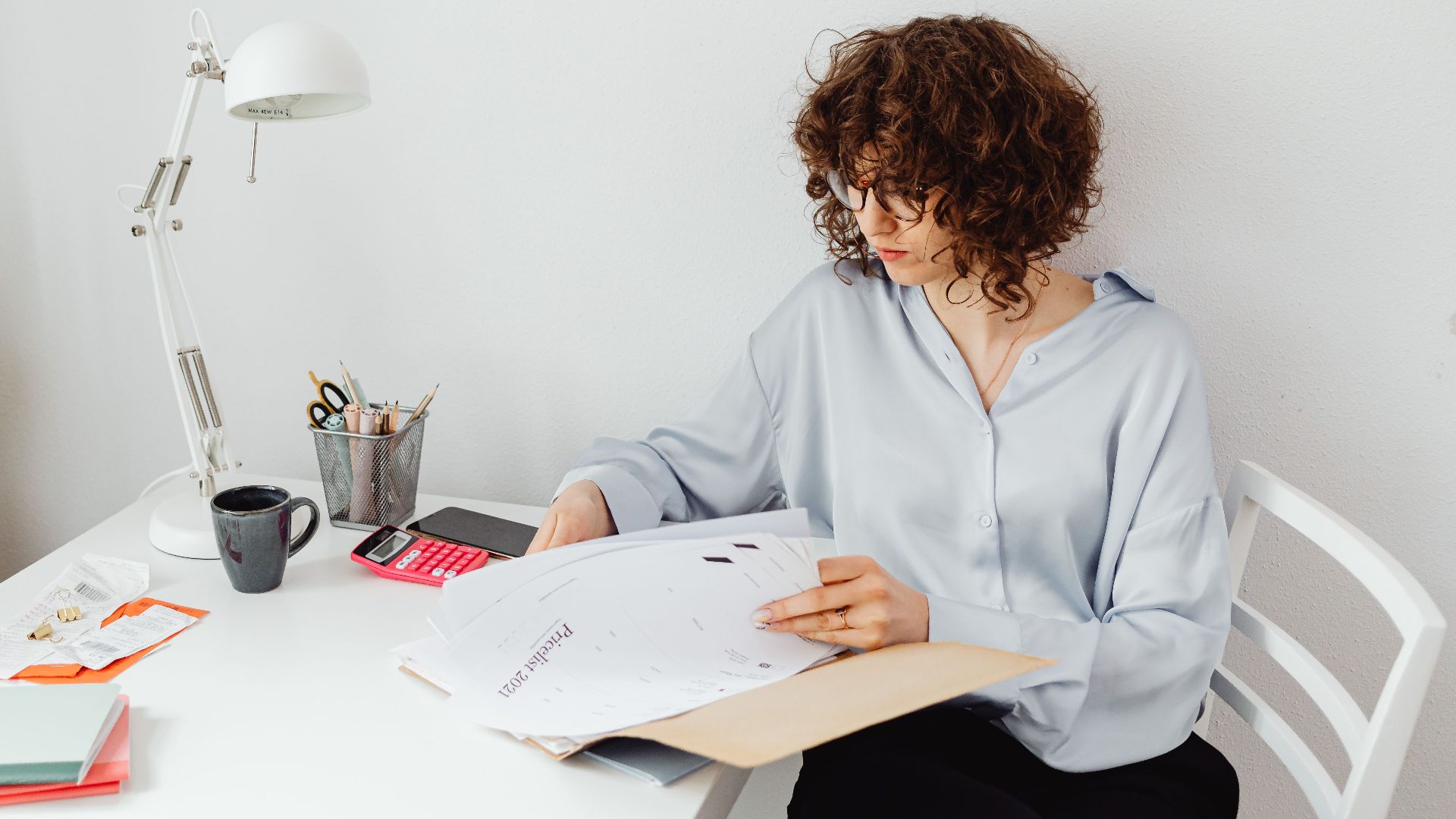 Woman reviewing documents in home office with plant and lamp.