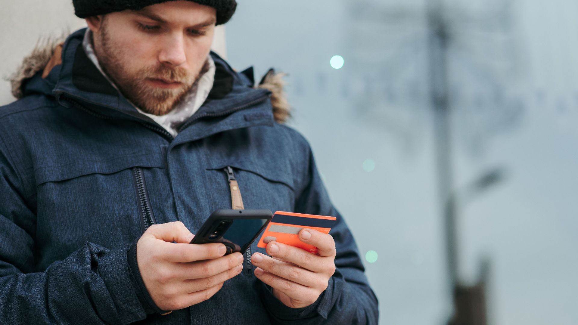 Crop concentrated man in warm clothes entering credentials of credit card on mobile phone while standing in street in daytime