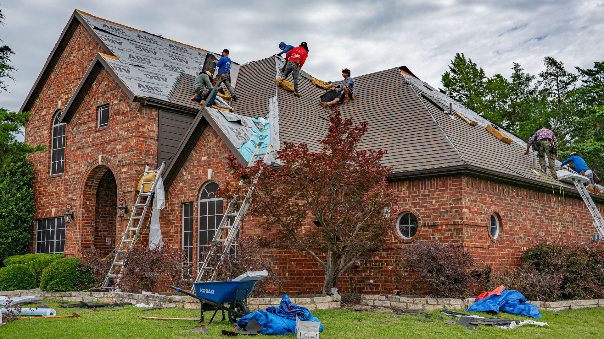 Roofers working on brick home in Allen, Texas, addressing shingles and roofing materials.