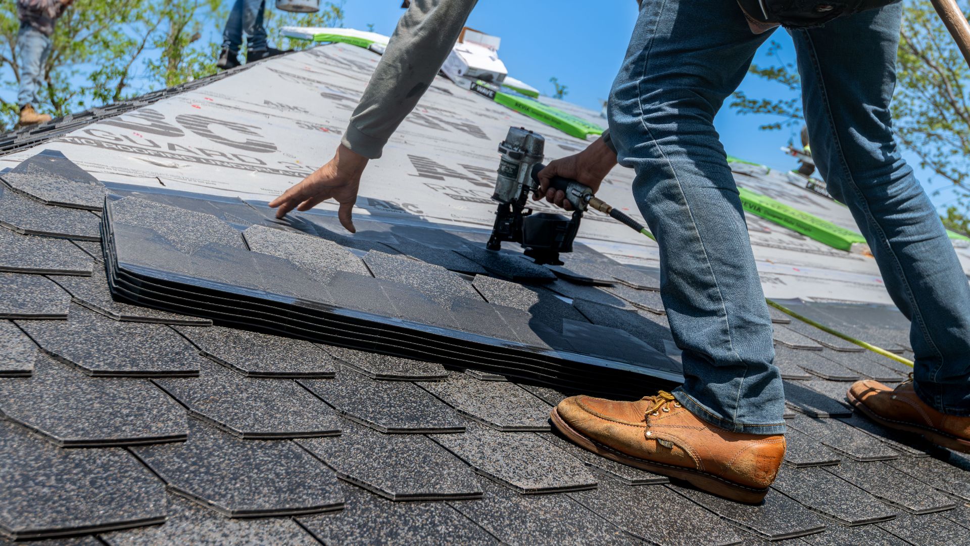 Roofer using nail gun for shingle installation on residential roof.