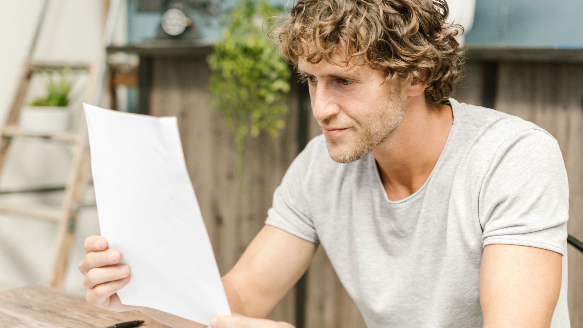 A man with curly hair evaluates documents at a desk, highlighting focused work in a professional setting.