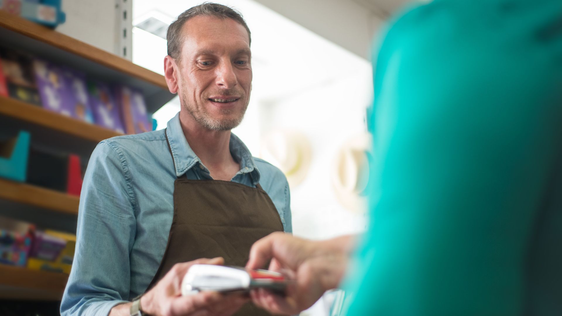A male store clerk assisting a customer with a payment transaction in a retail shop setting.