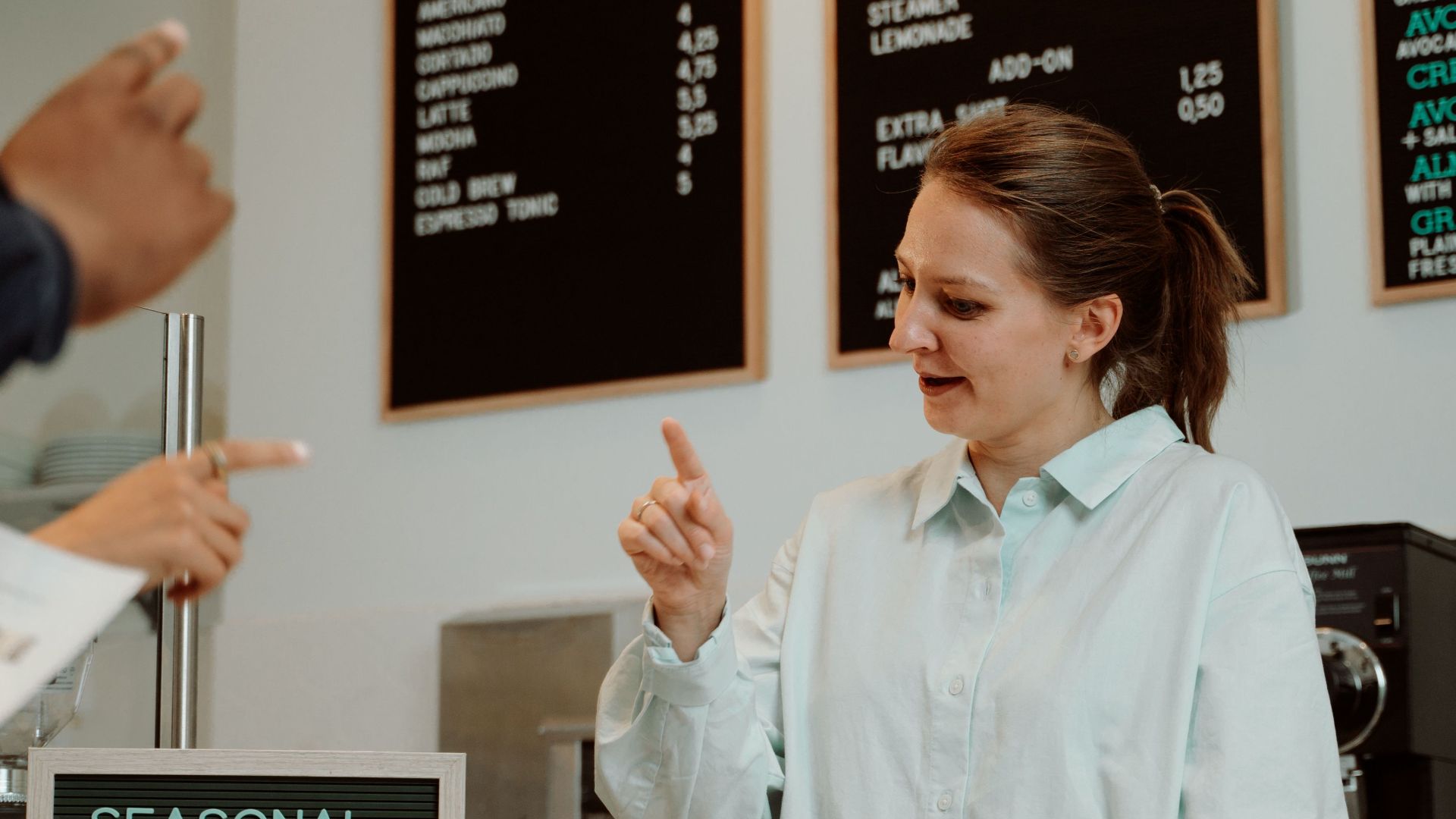 Barista serving customers at cafe counter with seasonal menu board.
