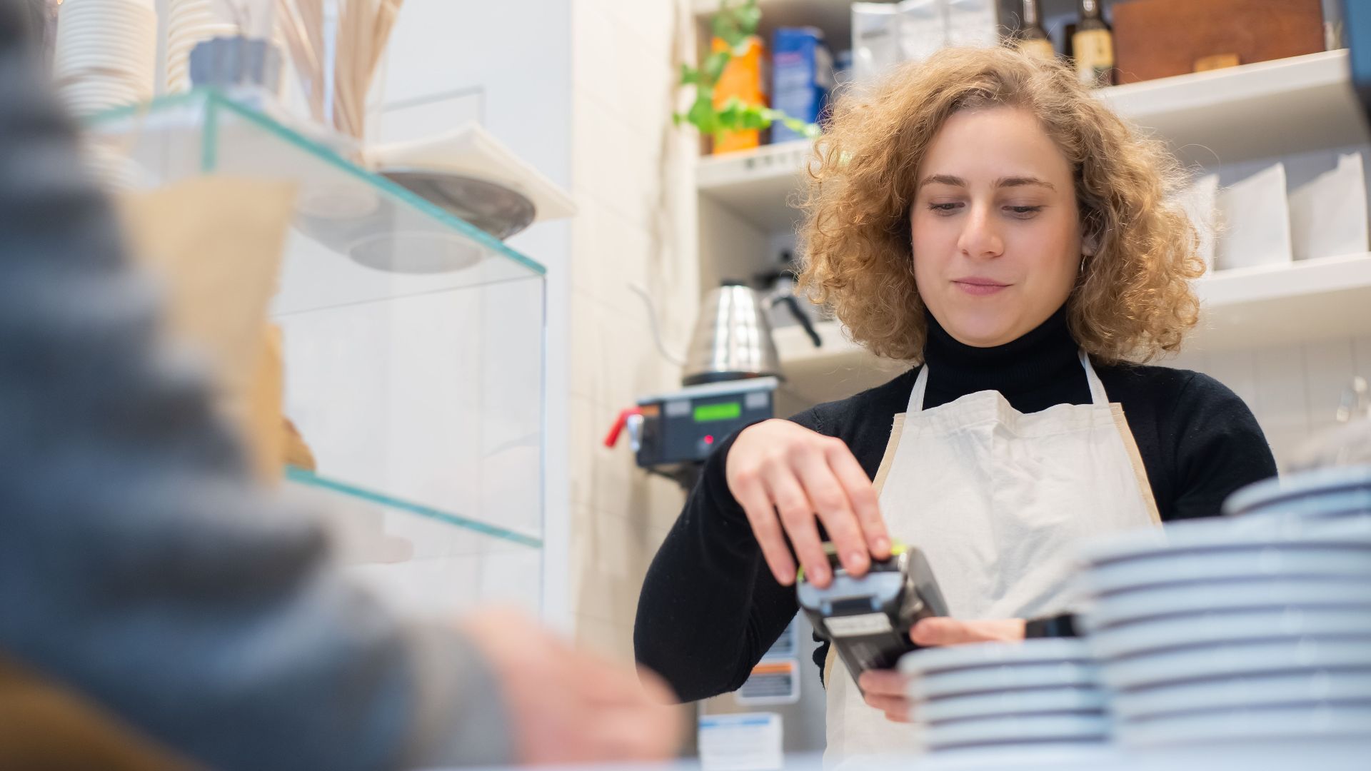 Barista wearing an apron processes a payment in a cozy Portuguese café.