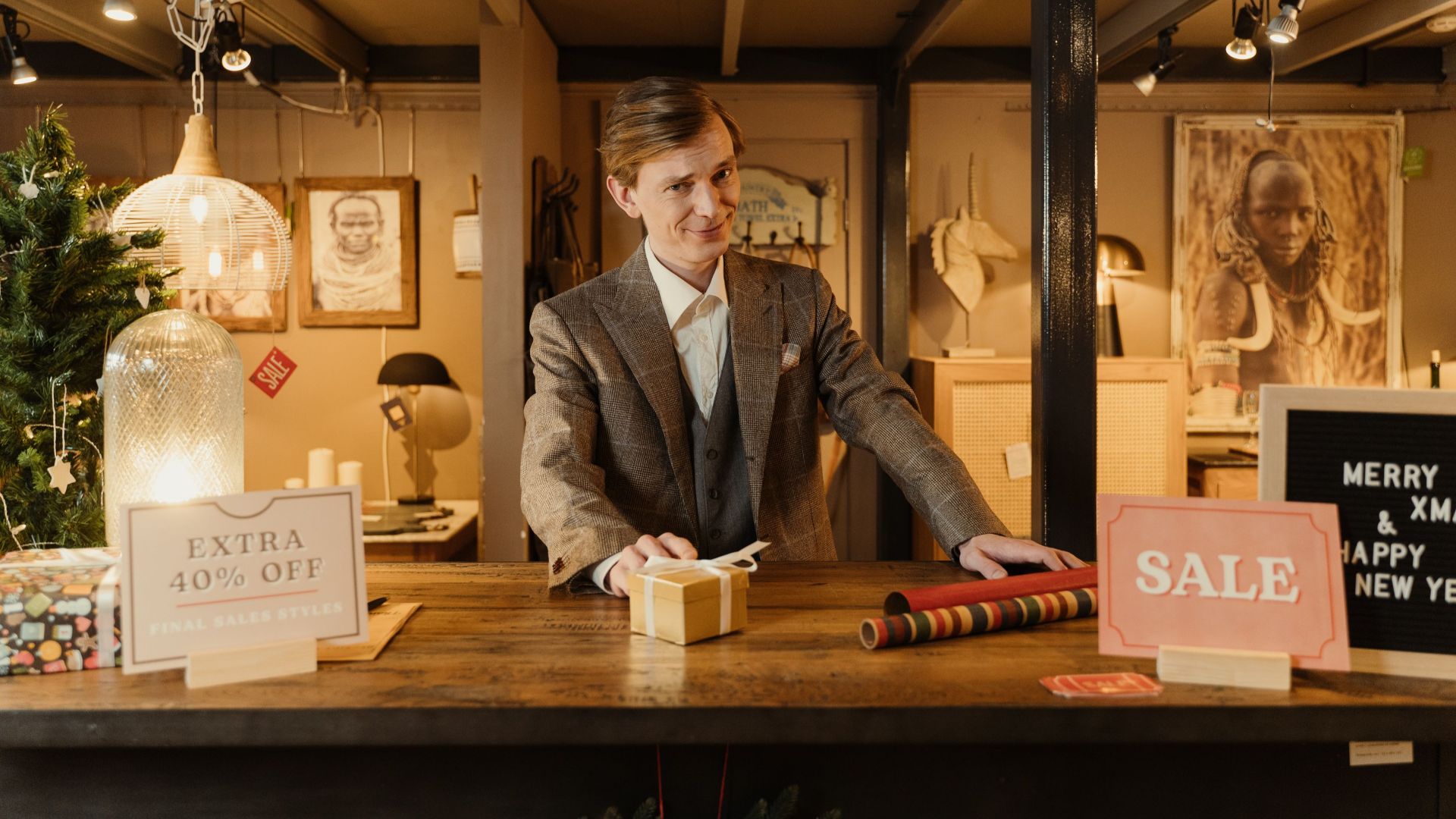Smiling salesman in a festive store with Christmas decor offering discounts and sales.