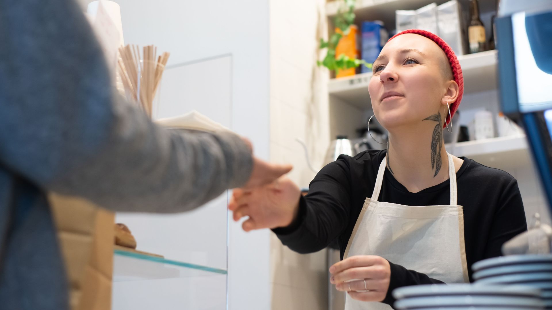 Barista with tattoos and red beanie serves a customer in a cozy Portugal café.