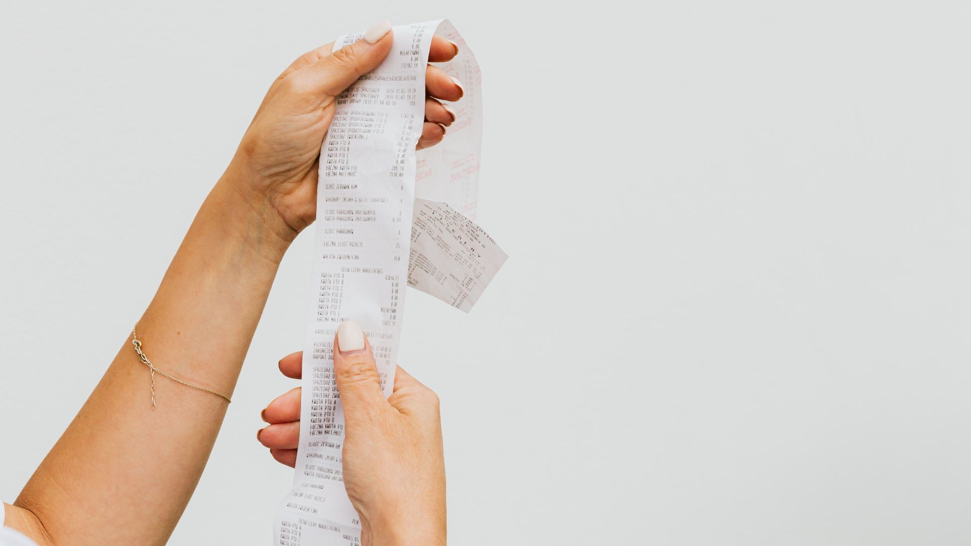 A detailed view of a person holding a long shopping receipt against a plain background.