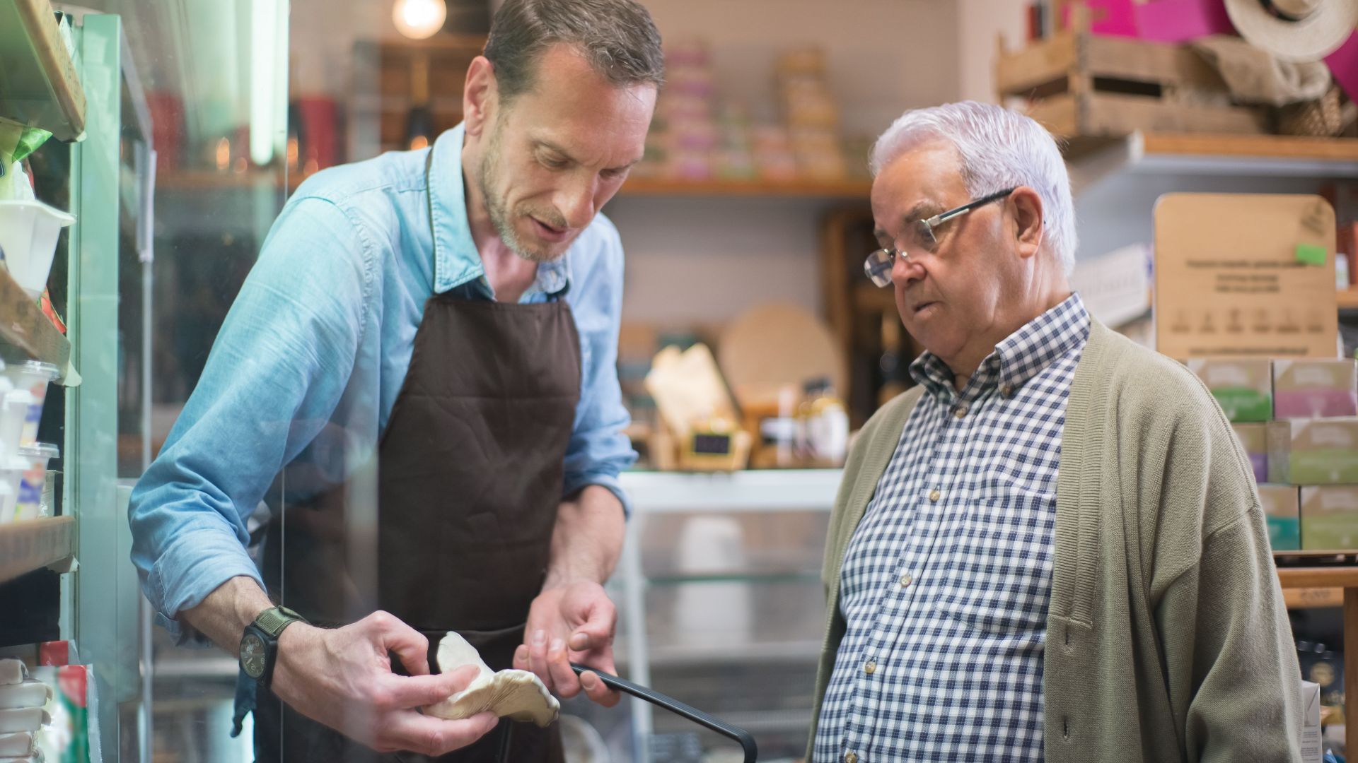 Friendly grocery store interaction between a salesman and senior customer in Portugal.