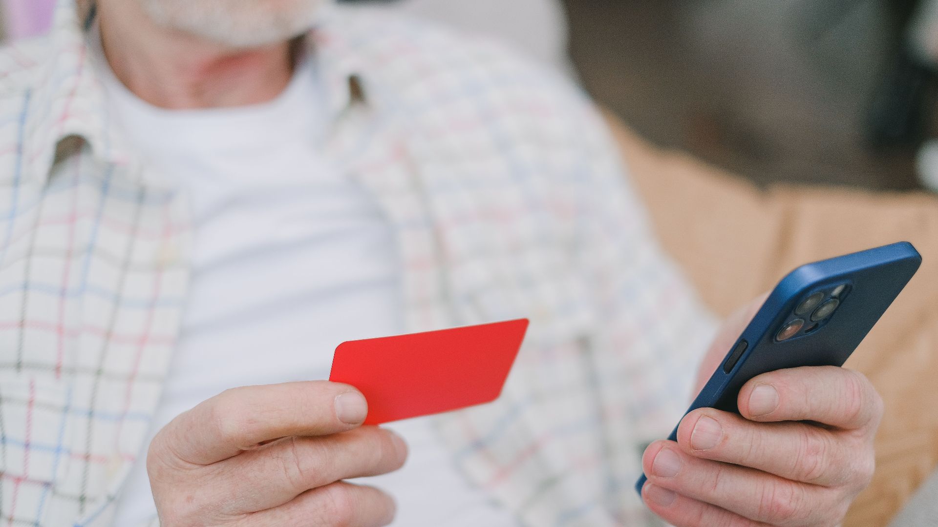 Close-up of a senior adult handling a card and smartphone for online payment.