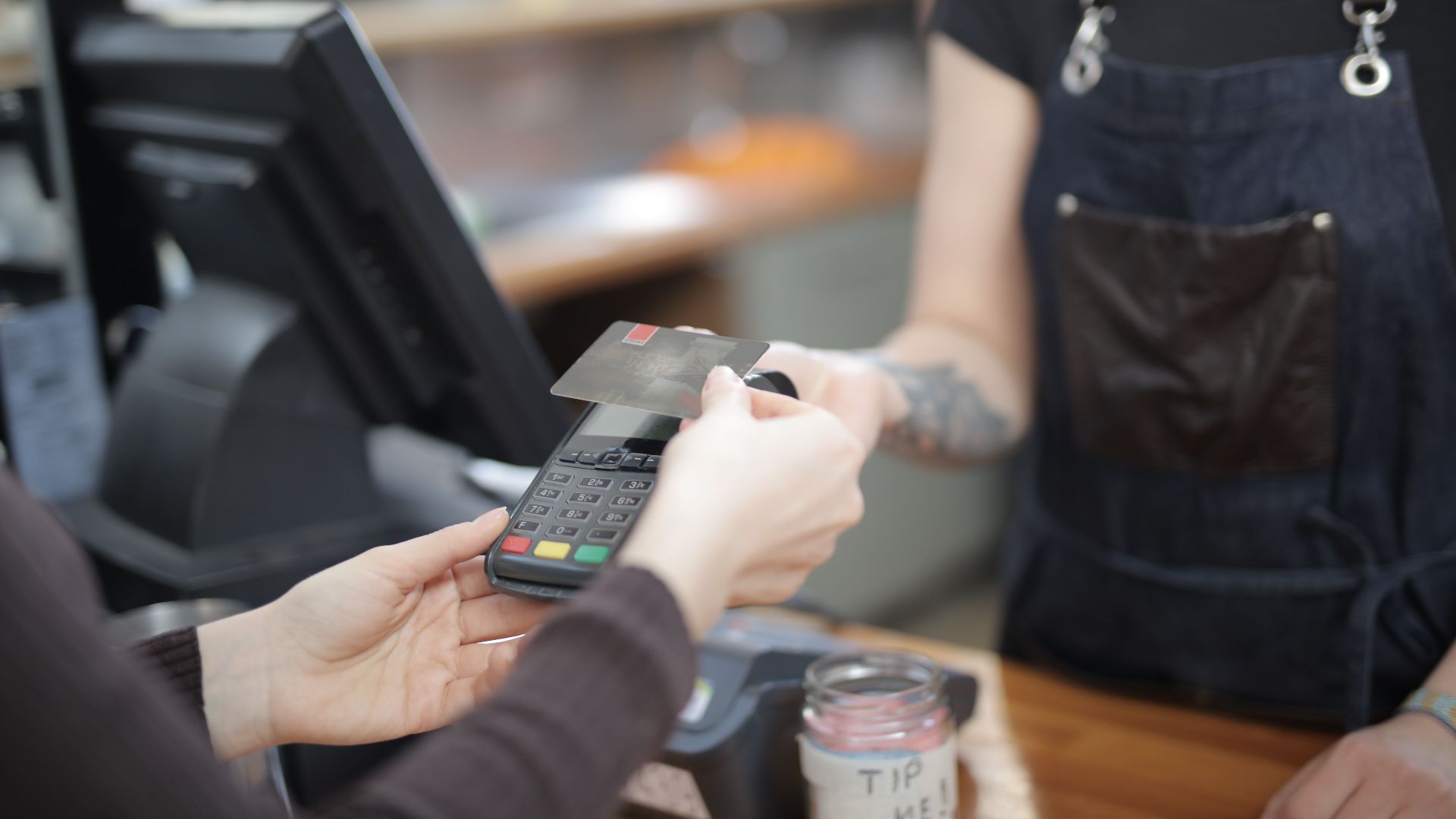 Close-up of customer and cashier during a credit card transaction at a store counter indoors.