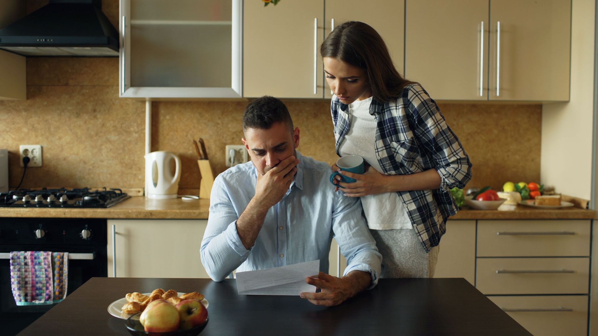 Concerned couple reviewing financial document in modern kitchen setting.