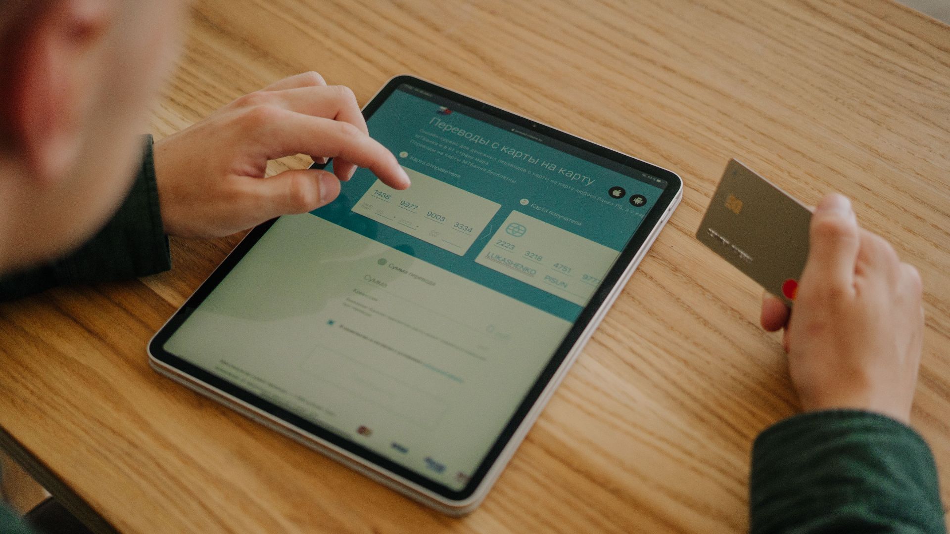 Person making an online payment using a tablet and credit card on a wooden desk.
