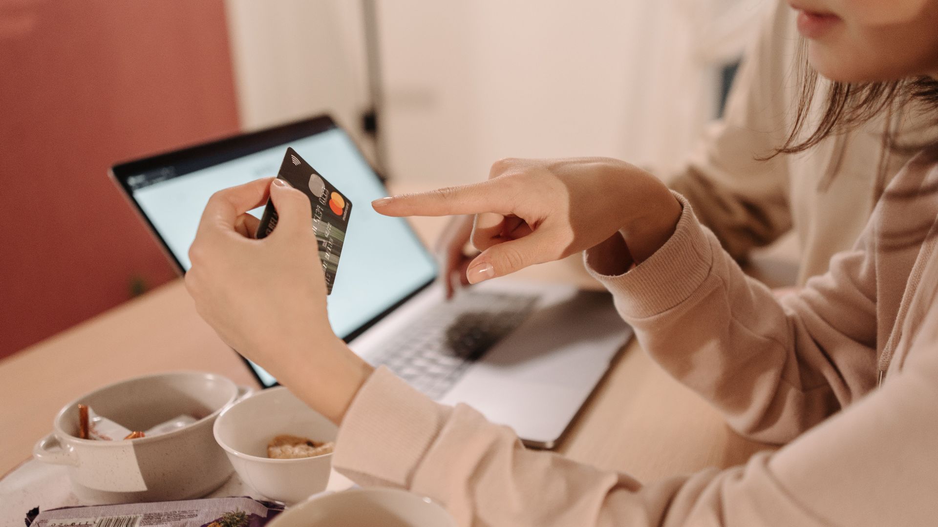 A woman using a credit card for online shopping while having tea and snacks on a table.