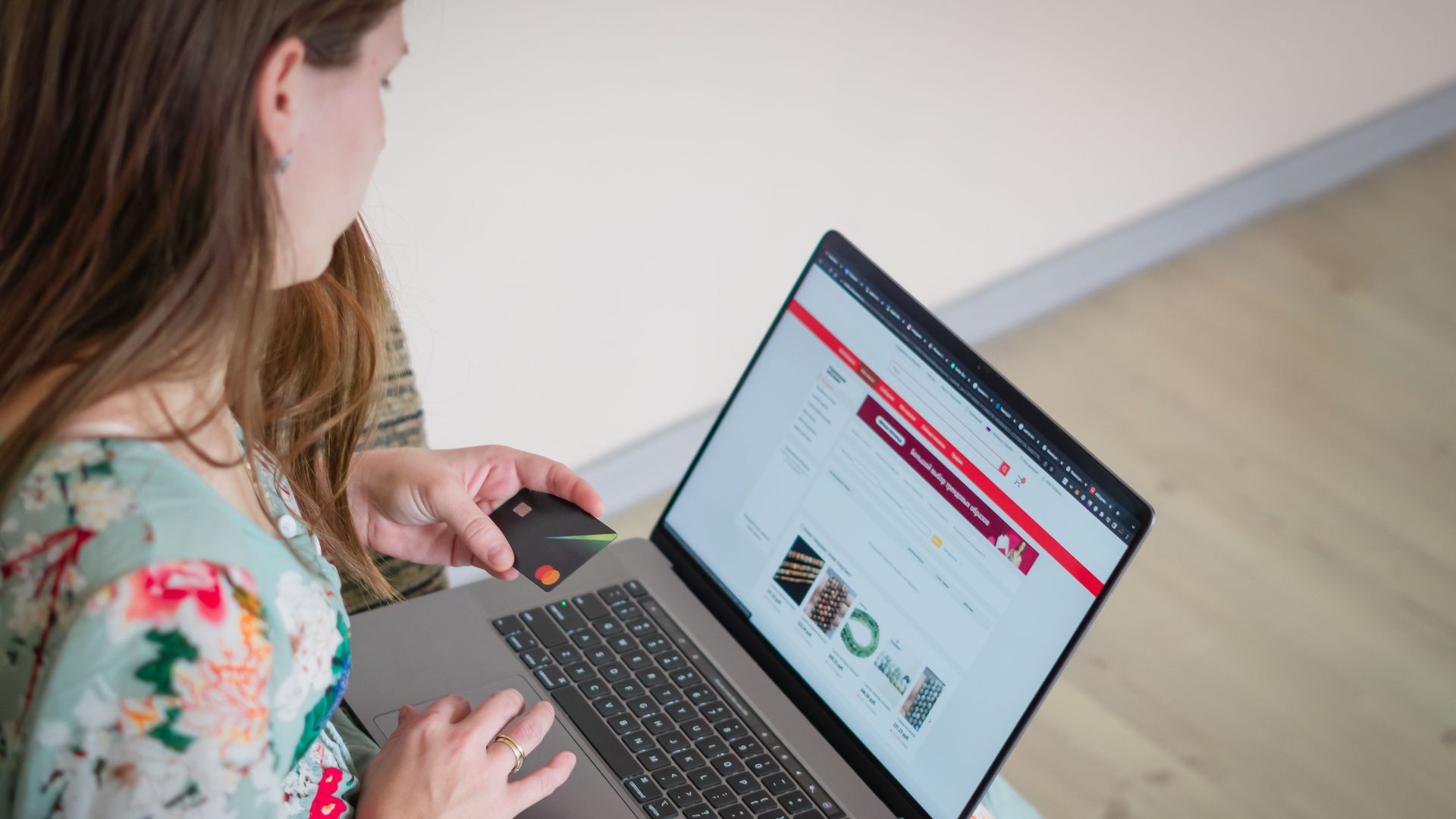Woman in floral dress shopping online with a laptop and credit card indoors.