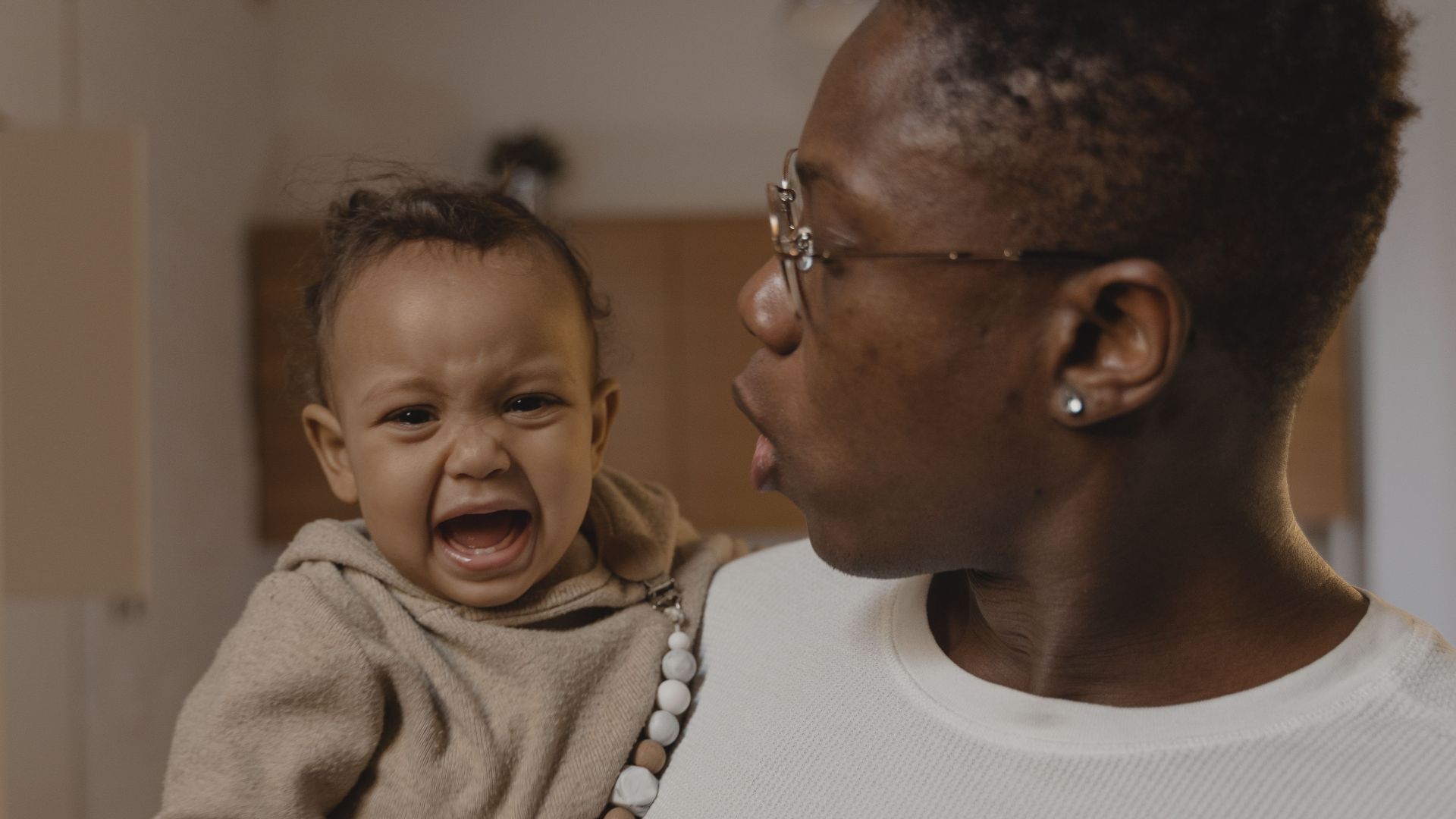 A father soothes his crying baby while holding them indoors.