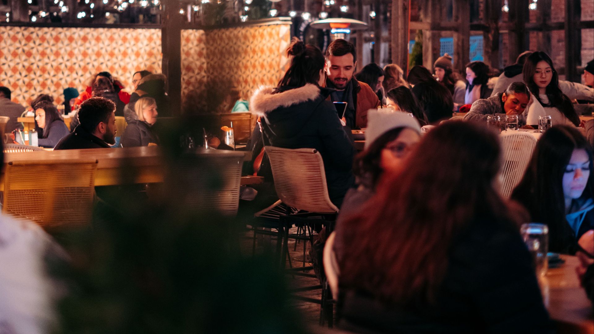Lively restaurant with people enjoying dinner under elegant lighting, capturing vibrant nightlife ambiance.