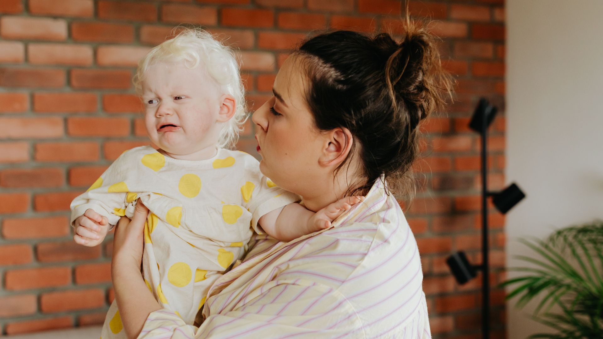 A caring mother comforts her crying albino baby in a cozy home setting.