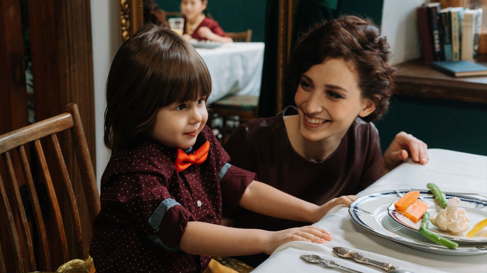 A mother and her son smiling during a meal in a fine dining setting, with healthy foods on the table.