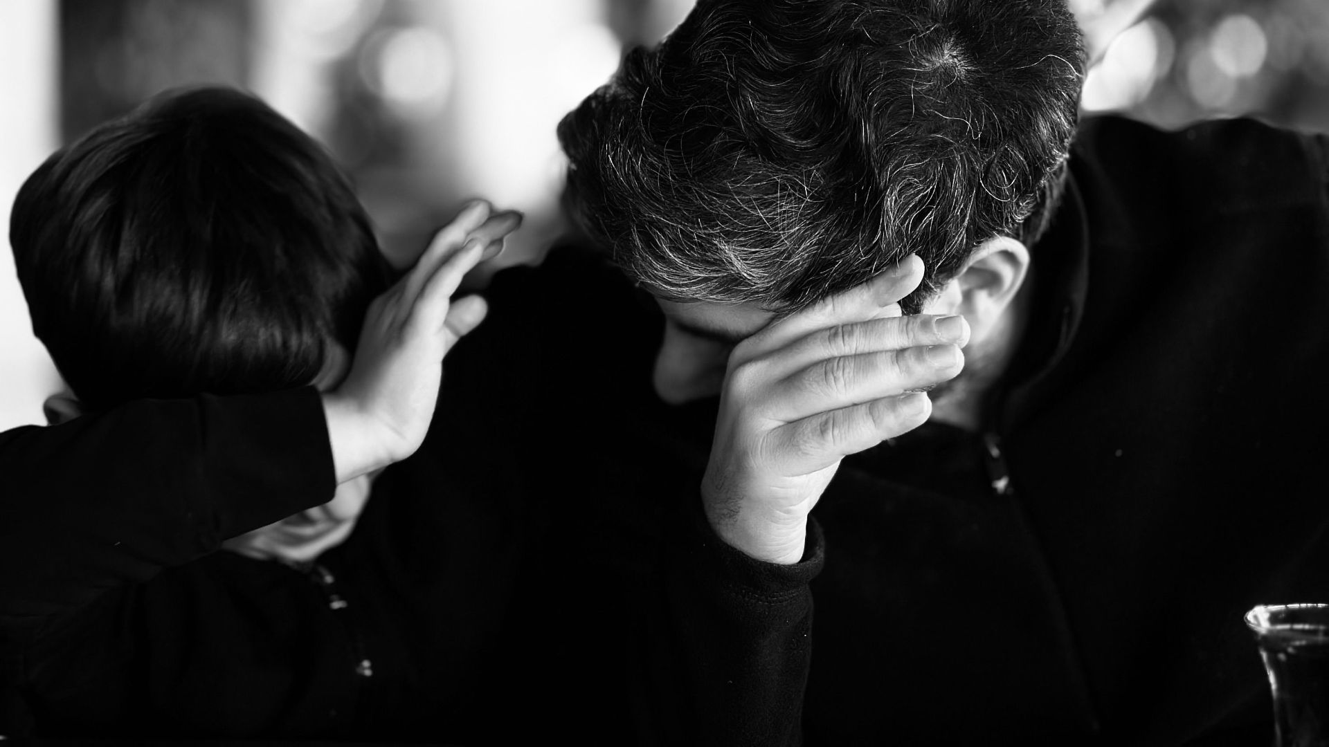 Emotionally candid father and son bonding in black and white indoors.