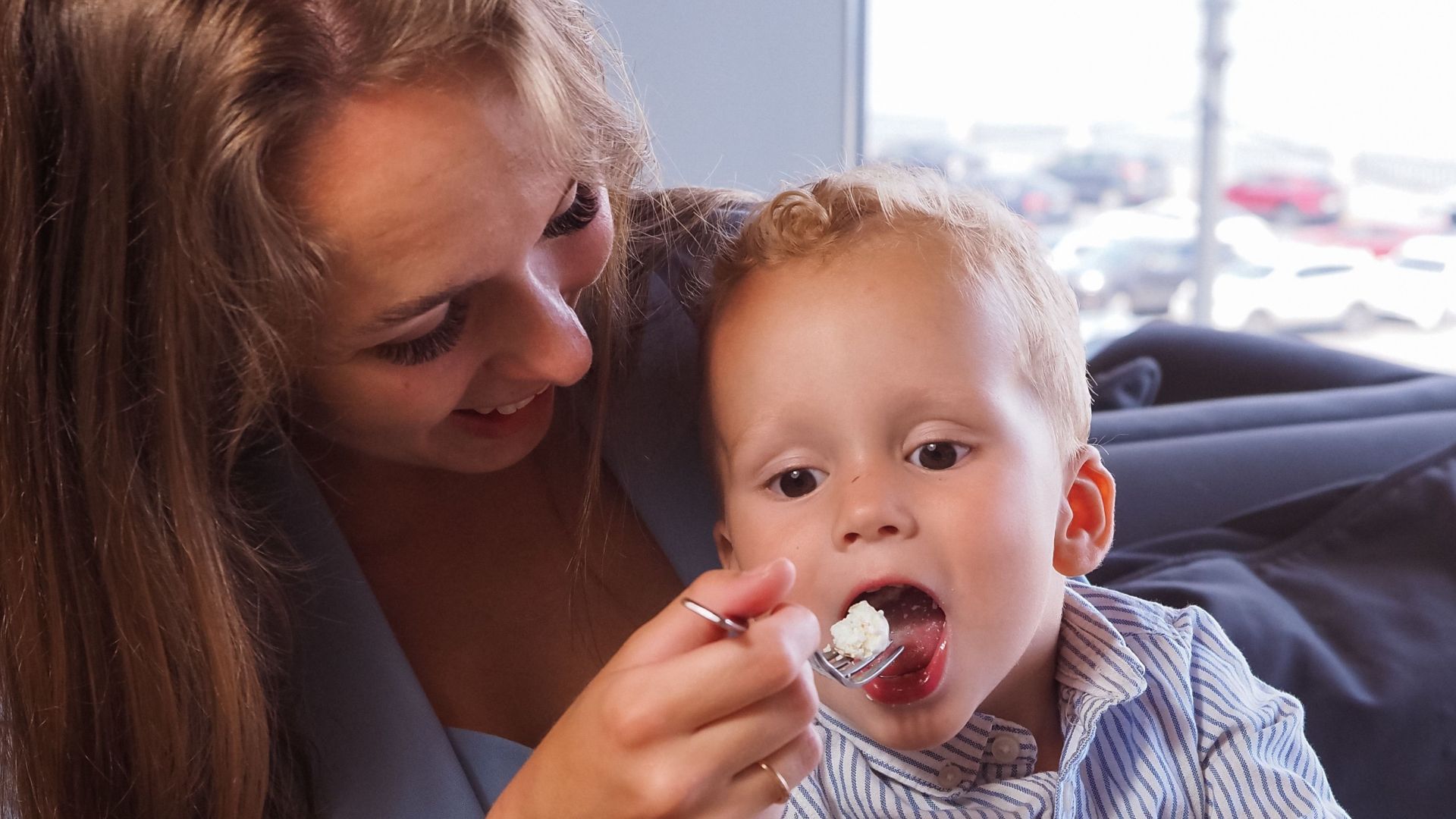 Mother lovingly feeds her child dessert, creating a warm family moment in a cozy cafe environment.