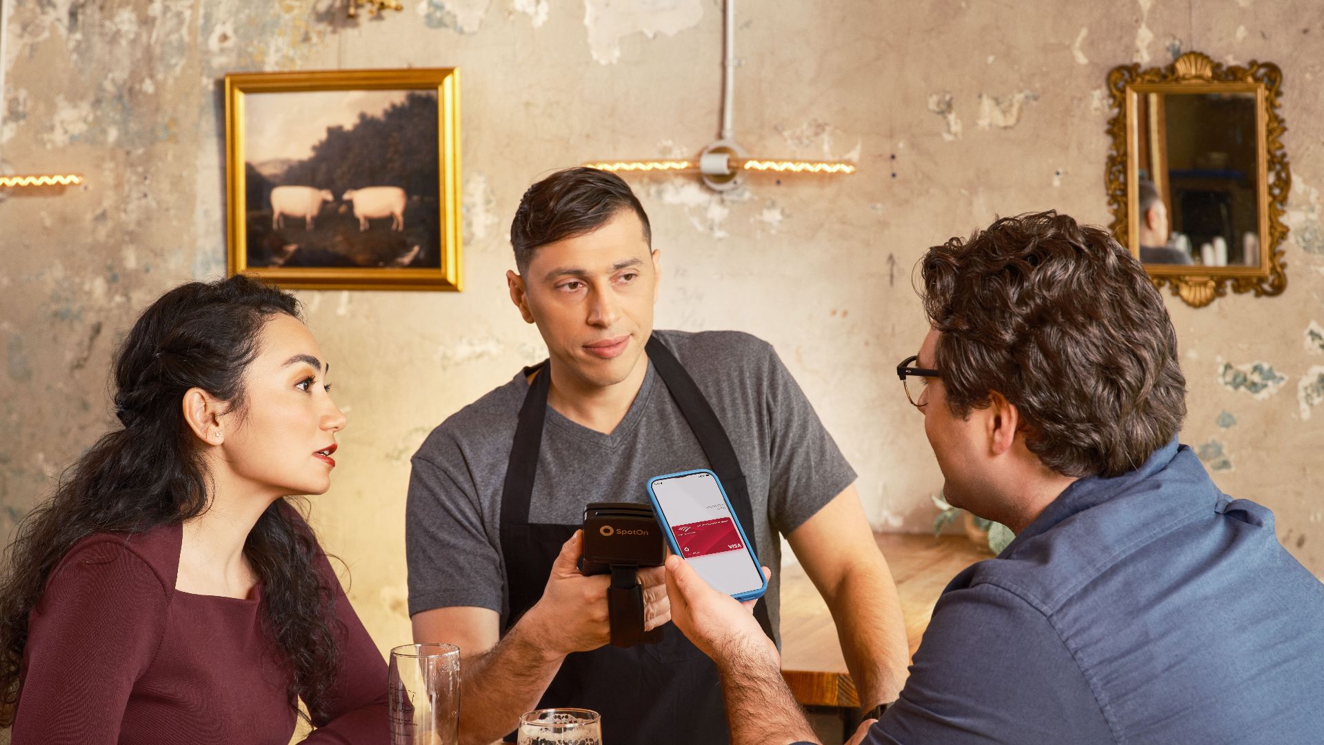 A couple makes a contactless payment using a smartphone at a restaurant bar counter.