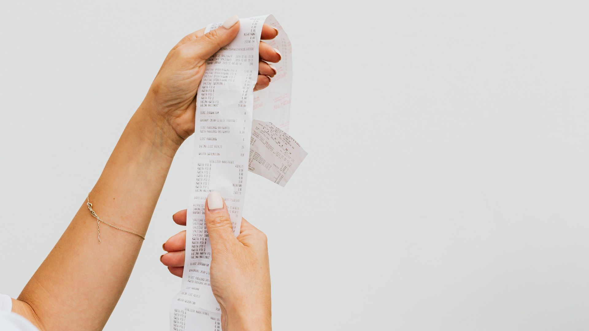 A detailed view of a person holding a long shopping receipt against a plain background.
