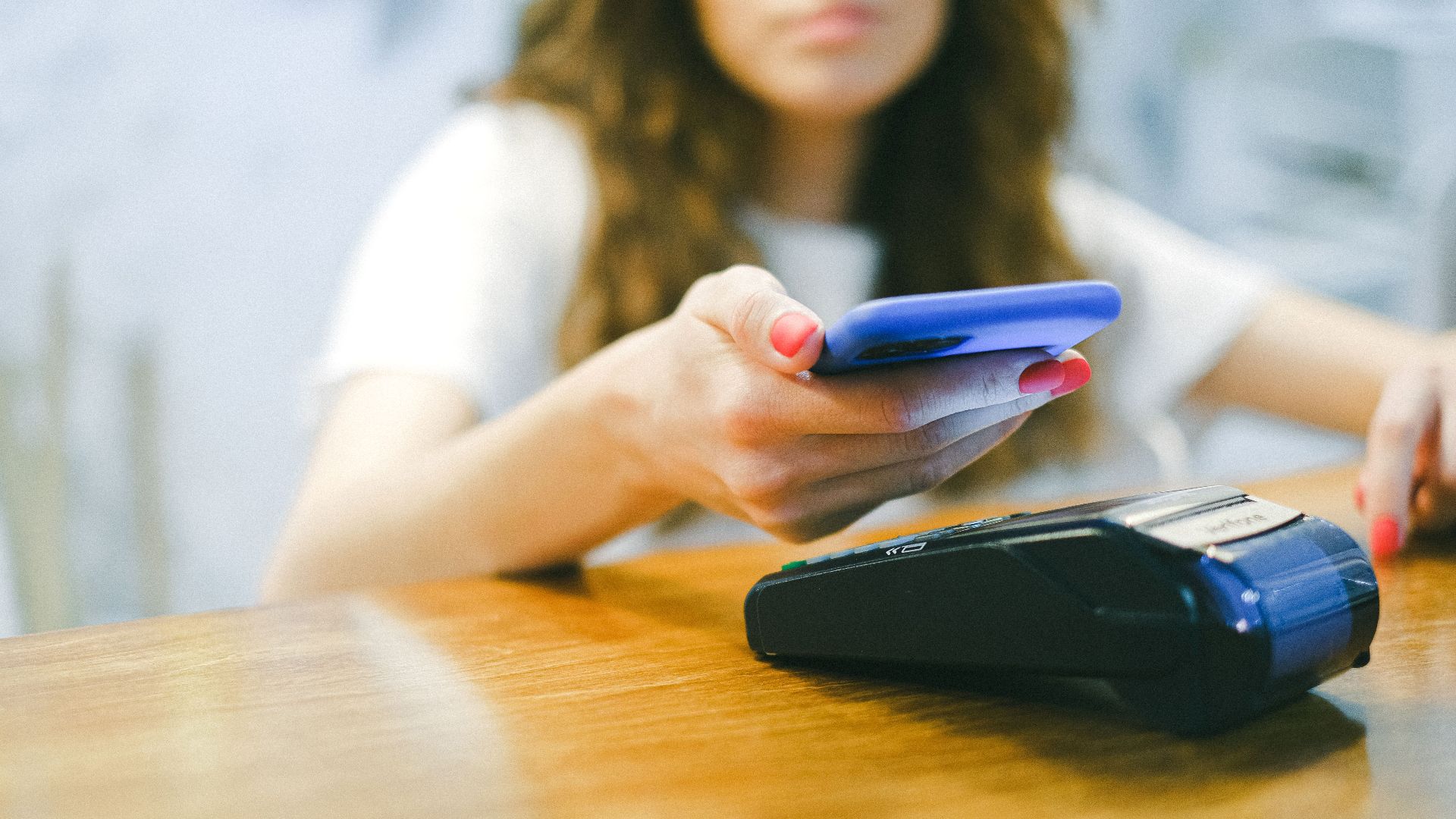 A woman processes a contactless payment using her smartphone at a payment terminal.