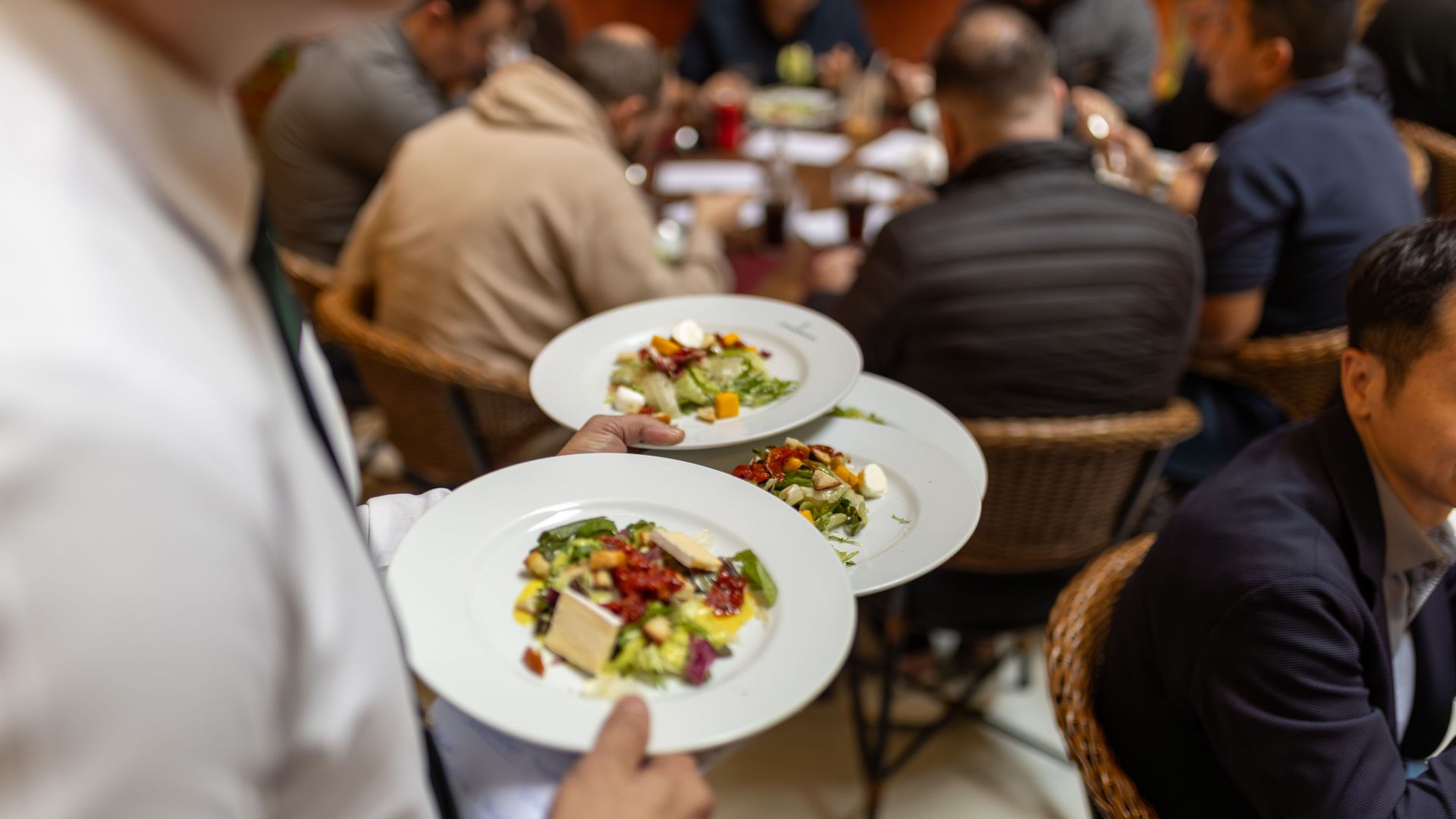 A waiter serves gourmet salads to a group of diners in a lively restaurant setting.