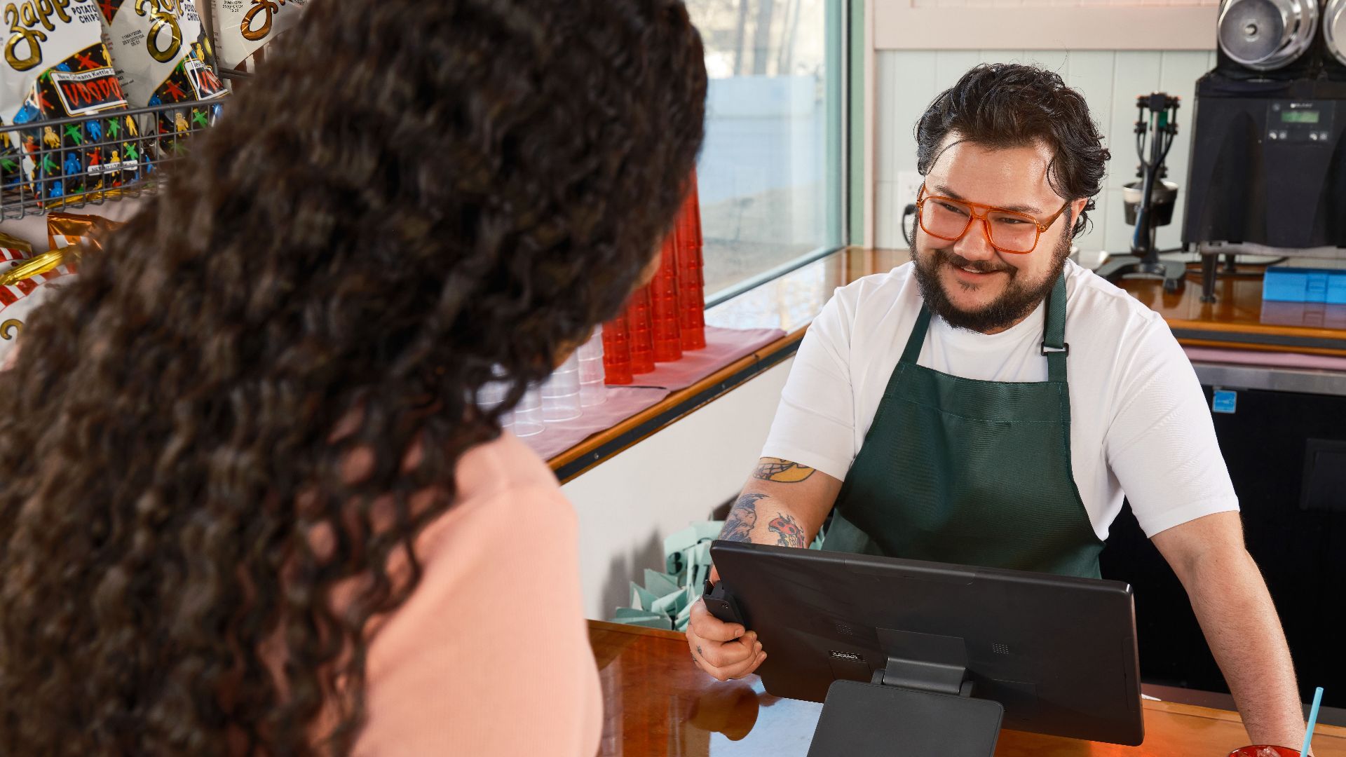 A customer uses contactless payment at a cafe counter, interacting with a cashier.