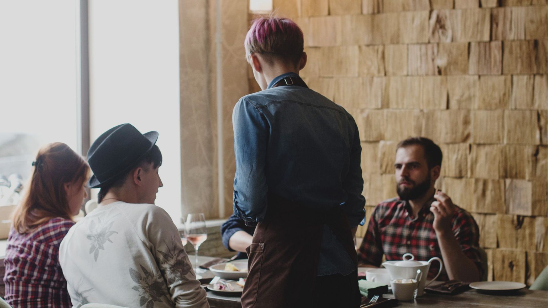 Anonymous male waiter wearing casual clothes standing near table with clients while listening attentively and accepting order