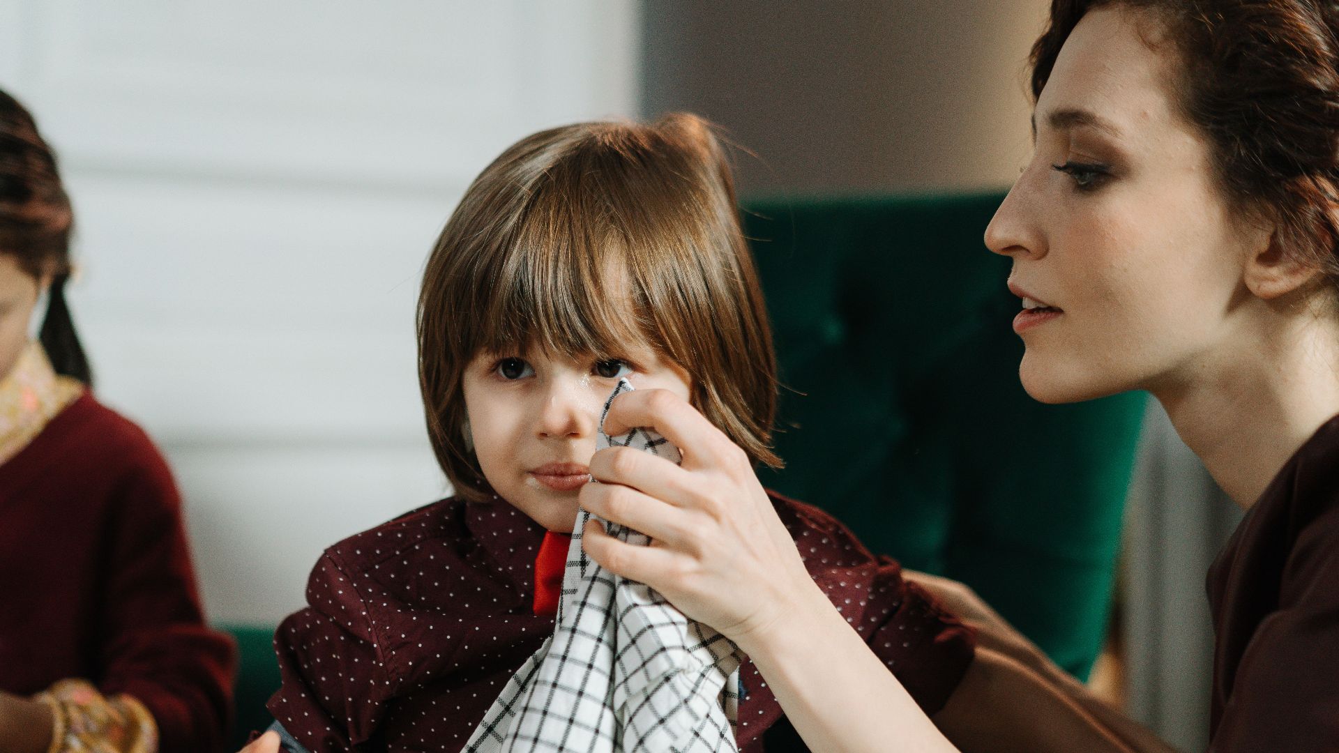 Woman assisting a child with a napkin during a meal indoors, highlighting care and family bonding.