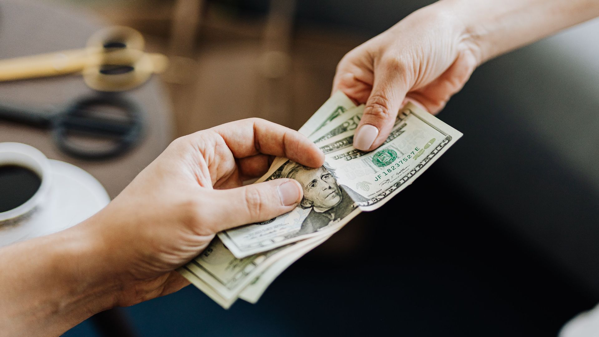 A close-up image of hands exchanging US dollar bills, symbolizing financial transaction or payment.