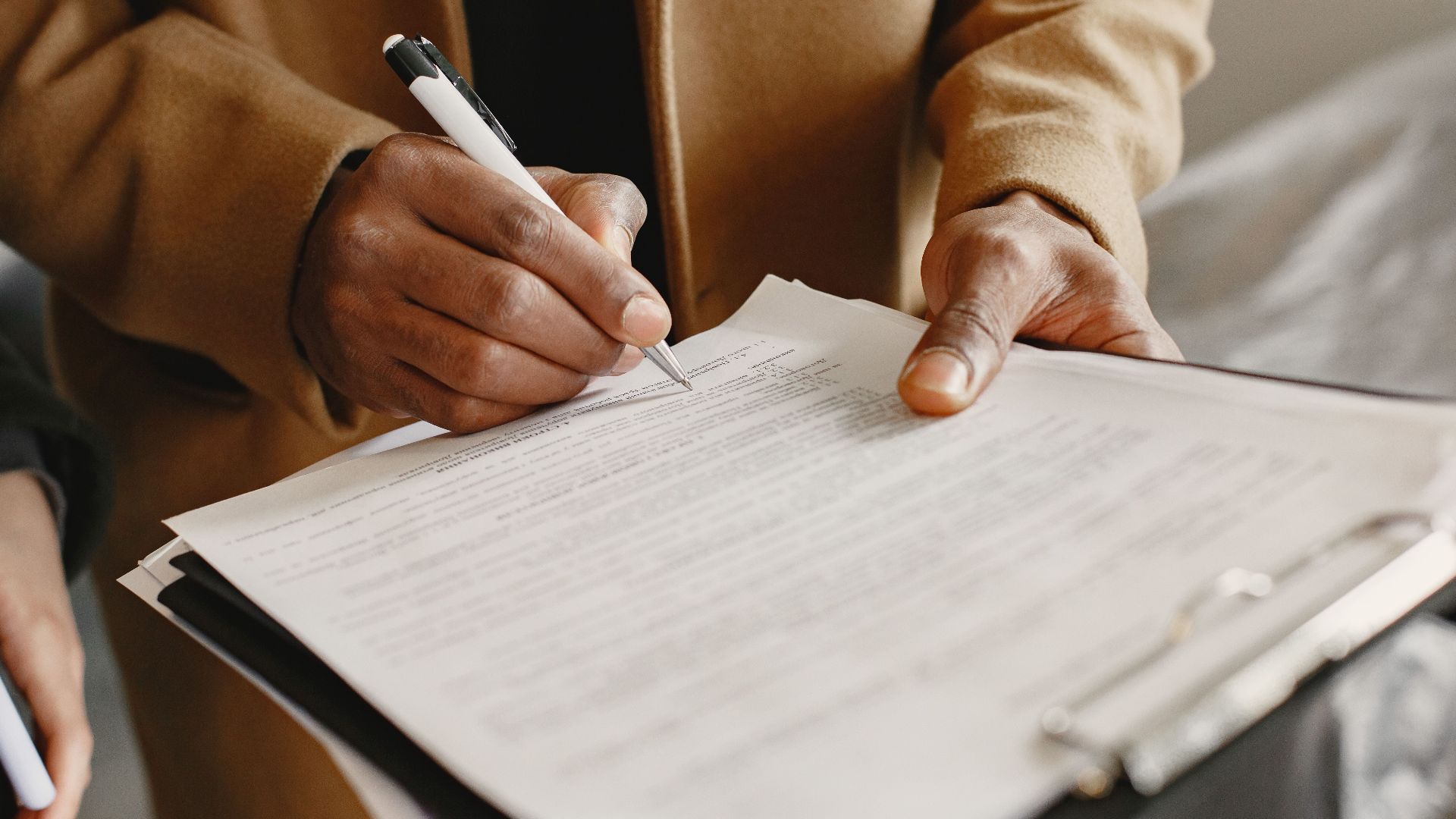 Close-up of a person signing a contract on a clipboard, focusing on legal formalities.