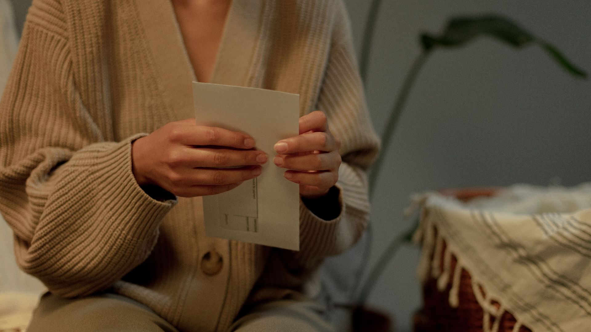 An adult holding a letter indoors, wearing a warm sweater, evoking a cozy mood.