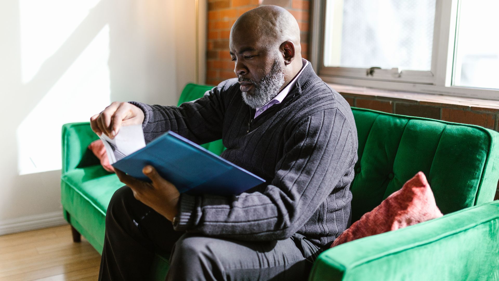 An adult man attentively reads papers on a vibrant green sofa in a well-lit room.